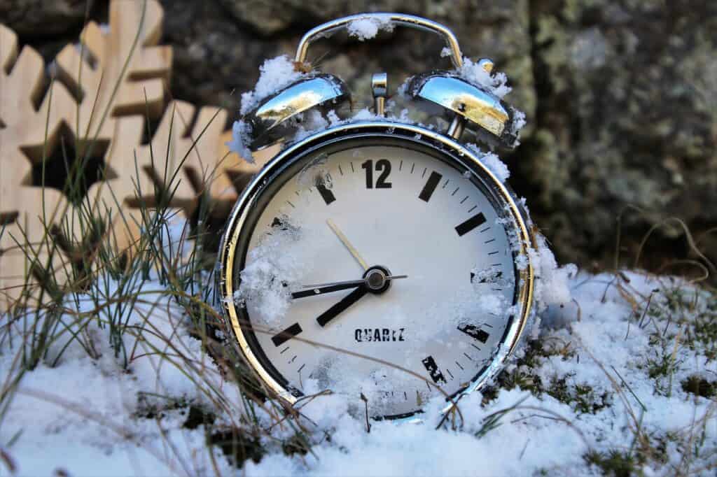 Zeitumstellung auf Winterzeit. Ein silberner Wecker im Schnee.
