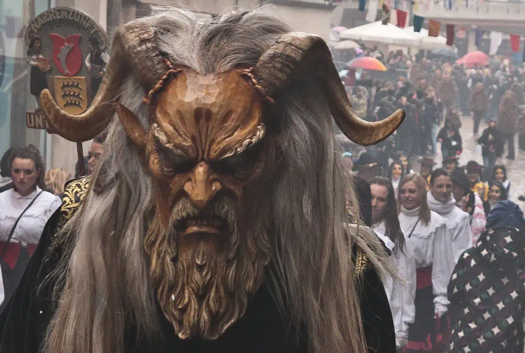 Ein als Dämon verkleideter Mann mit langen Haaren und Hörnern, der an Faschingsfeierlichkeiten in Österreich teilnimmt.