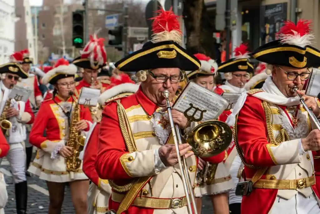 Eine lebhafte Faschingsgruppe von Männern in roten Uniformen, die auf einer Straße in Österreich Instrumente spielen.